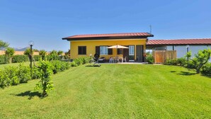 Una casa amarilla con techo rojo, un patio con mobiliario exterior y un césped bien cuidado.