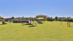 A spacious outdoor area with a grassy lawn, several lounge chairs, a small pool, and a building with a red roof.