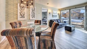 A modern living room with a glass dining table, patterned armchairs, a sofa, and a large window offering a view of a snowy landscape. - Mountain Nest Retreat Ground Level Condo Brian Head (Brian Head)