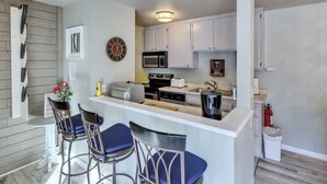 A compact kitchen with white cabinets, a microwave, a toaster, and a sink. There are three blue bar stools and a small decorative clock on the wall. - Mountain Nest Retreat Ground Level Condo Brian Head (Brian Head)