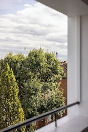 A view from a window overlooking a tree-lined street with a clear sky and a distant tower. - Lux Regents Park 2 bed 2 bath flat with AC (London)