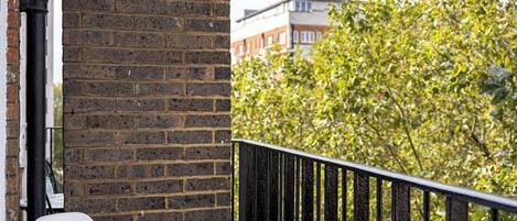 A balcony with a brick wall, a black railing, and two chairs.