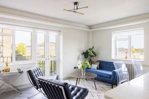 A modern living room with a blue sofa, a black leather chair, and a round table with a vase of flowers. - Lux Regents Park 2 bed 2 bath flat with AC (London)