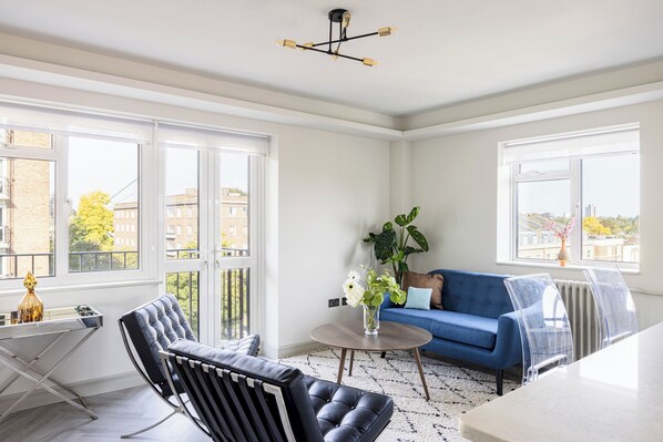 A modern living room with a blue sofa, a black leather chair, and a round table with a vase of flowers. - Lux Regents Park 2 bed 2 bath flat with AC (London)