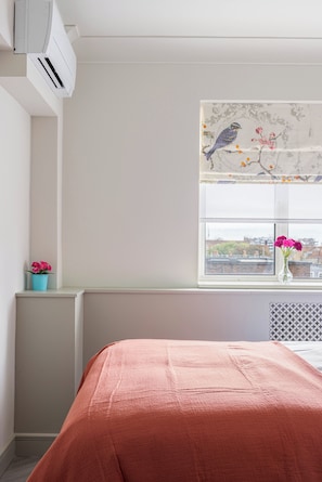 A room with a bed, a window with a view, a radiator, and a small blue pot with flowers. - Lux Regents Park 2 bed 2 bath flat with AC (London)
