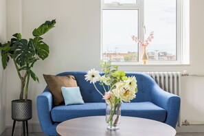 A room with a blue sofa, a round table, a potted plant, and a vase with flowers. - Lux Regents Park 2 bed 2 bath flat with AC (London)