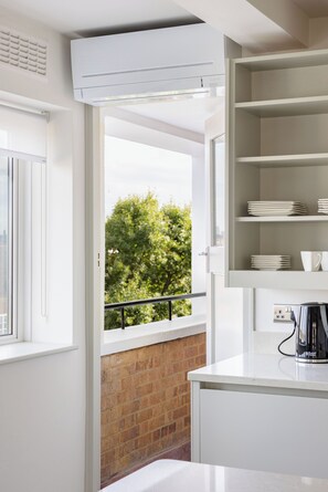 A modern kitchen with white cabinetry, a built-in stove, and a window overlooking a brick wall and greenery. - Lux Regents Park 2 bed 2 bath flat with AC (London)