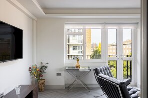 A modern living room with a glass table, a sofa, a TV mounted on the wall, and a view of buildings through large windows. - Lux Regents Park 2 bed 2 bath flat with AC (London)