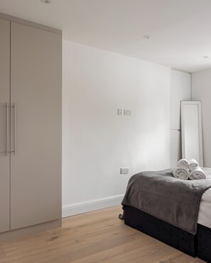 A bedroom with a wardrobe, a bed with a grey blanket, and a mirror on the wall. - Picktheplace Kensington Lux Apartments III (London)