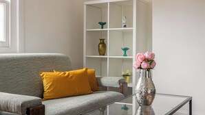 A living room with a grey sofa, a yellow pillow, a glass coffee table, and a white shelving unit with decorative items. - Picktheplace Kensington Lux Apartments III (London)