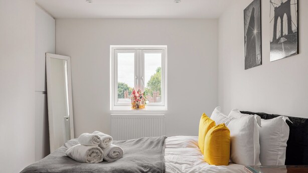 A bedroom with a bed, a window, a radiator, and a nightstand. - Picktheplace Kensington Lux Apartments III (London)