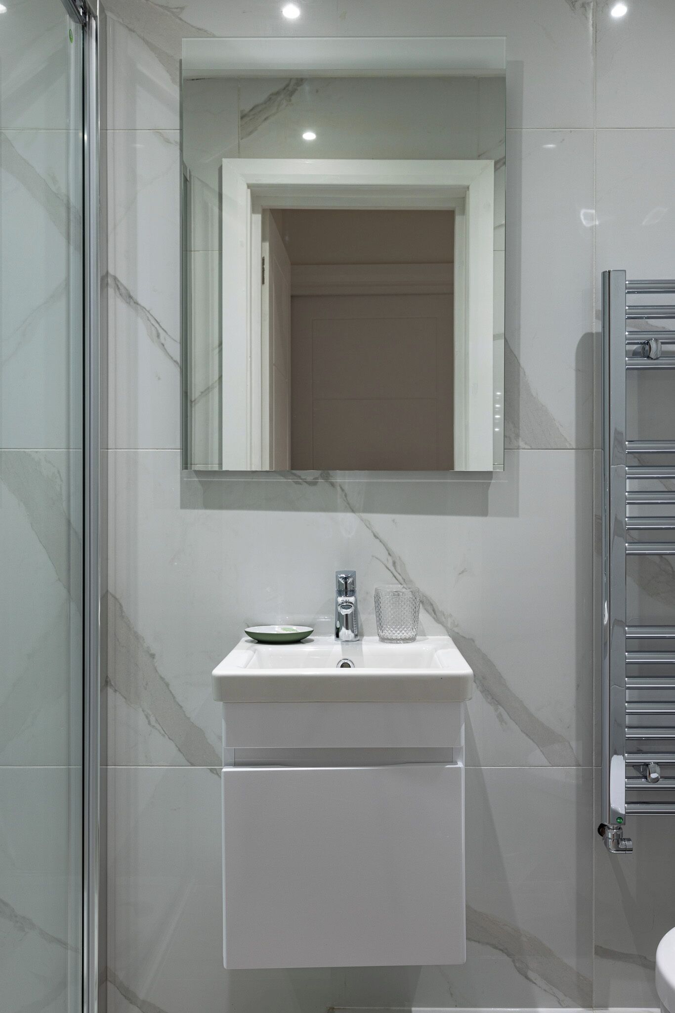 Une salle de bain avec une douche à parois de verre, un lavabo blanc doté d’un plan de toilette en marbre et un porte-serviettes.