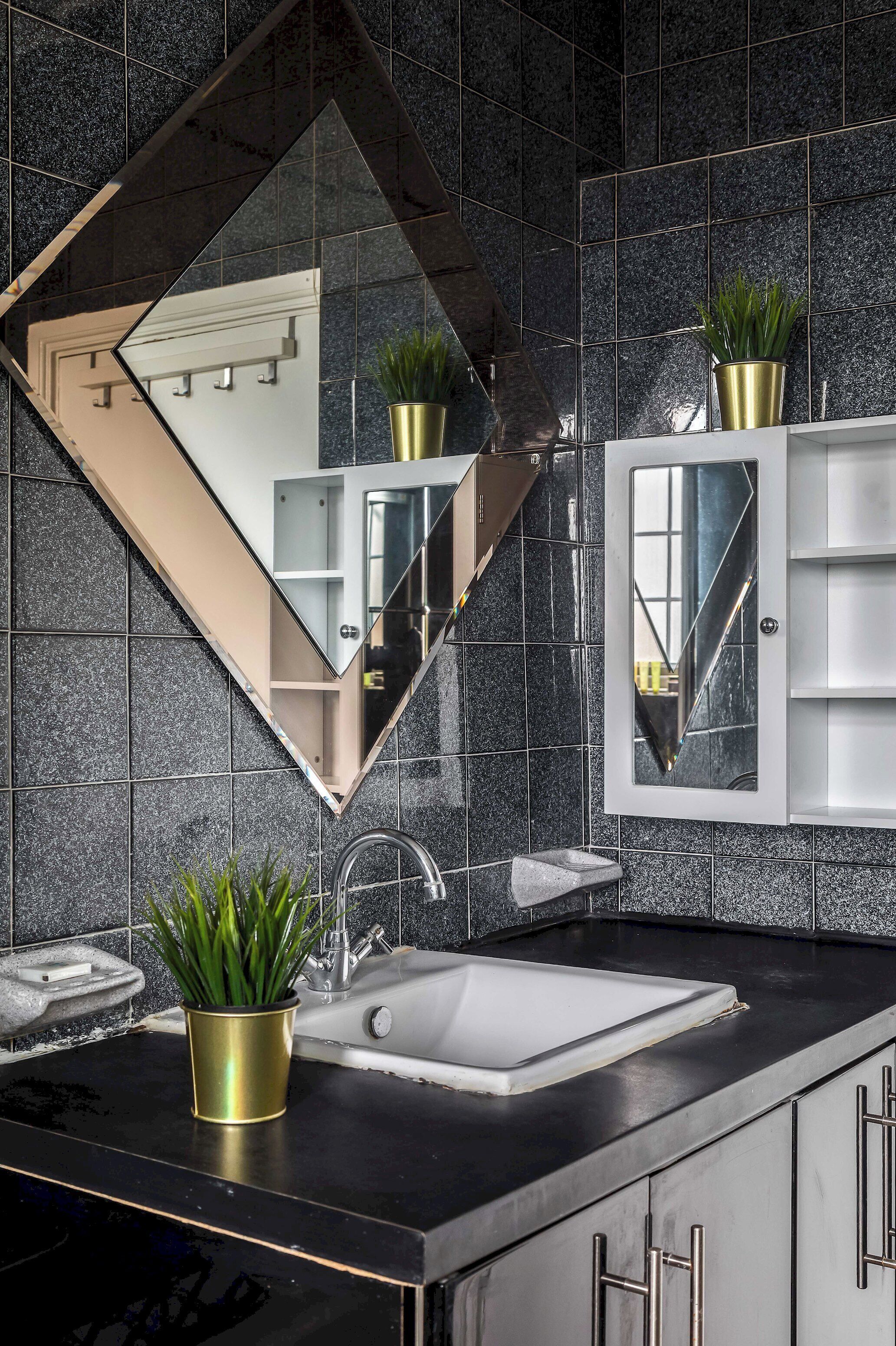A modern bathroom with a black countertop, a white sink, and a large mirror. There are two potted plants on the counter.