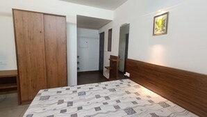 A bedroom with a bed, wooden wardrobe, a mirror, and a door leading to a bathroom.