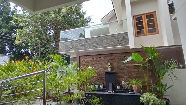 A modern house with a balcony, a stone wall, and various potted plants.