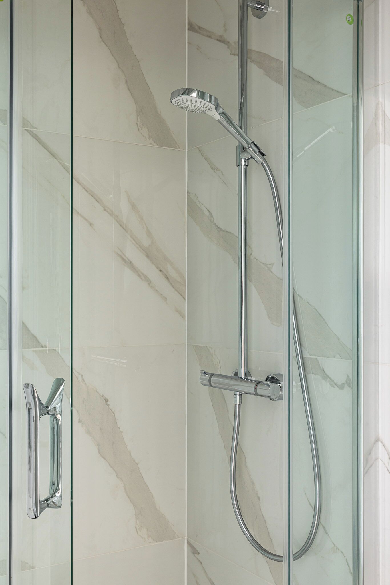 Une douche fermée par des parois en verre, dotée d’un pommeau de douche à main et d’un flexible.
