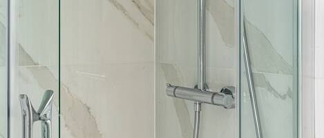 Une douche fermée par des parois en verre, dotée d’un pommeau de douche à main et d’un flexible.