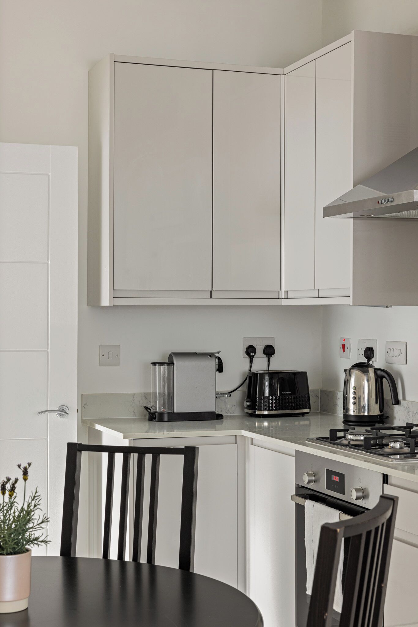 Une cuisine moderne avec des meubles blancs, un plan de travail noir, un grille-pain, une bouilloire et une cuisinière.