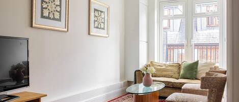 A living room with a flat-screen TV, a glass coffee table, a sofa, and a red patterned rug.