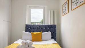 Una cama bien tendida con toallas enrolladas, una ventana con persianas y cuadros en la pared.