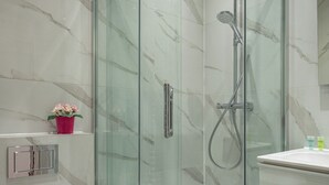 Un baño moderno con ducha de vidrio, un lavabo blanco y una pared con azulejos de mármol.