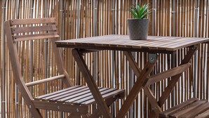 A wooden table and chairs set against a bamboo fence.