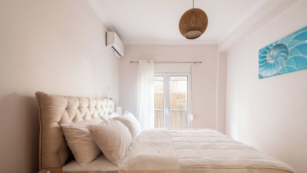 A bedroom with a large bed, a hanging light fixture, a window with a view, and a wall-mounted air conditioner.