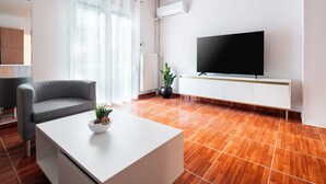A modern living room with a flat-screen TV, a grey sofa, a white coffee table, and a potted plant.