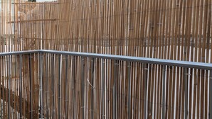 A corner of a room with a bamboo fence and metal railing, tiled floor, and a white wall with a window.