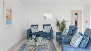 A modern living room with two blue sofas, a glass coffee table, and a large plant. - Estuary View -  Secure Parking - Nearby Beach (Teignmouth)