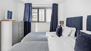 A bedroom with a bed, a dresser, a window with curtains, and a bedside lamp. - Estuary View -  Secure Parking - Nearby Beach (Teignmouth)