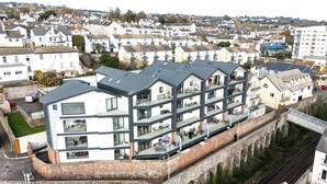 A modern multi-story building with balconies, located near a railway track and surrounded by traditional houses. - Estuary View -  Secure Parking - Nearby Beach (Teignmouth)