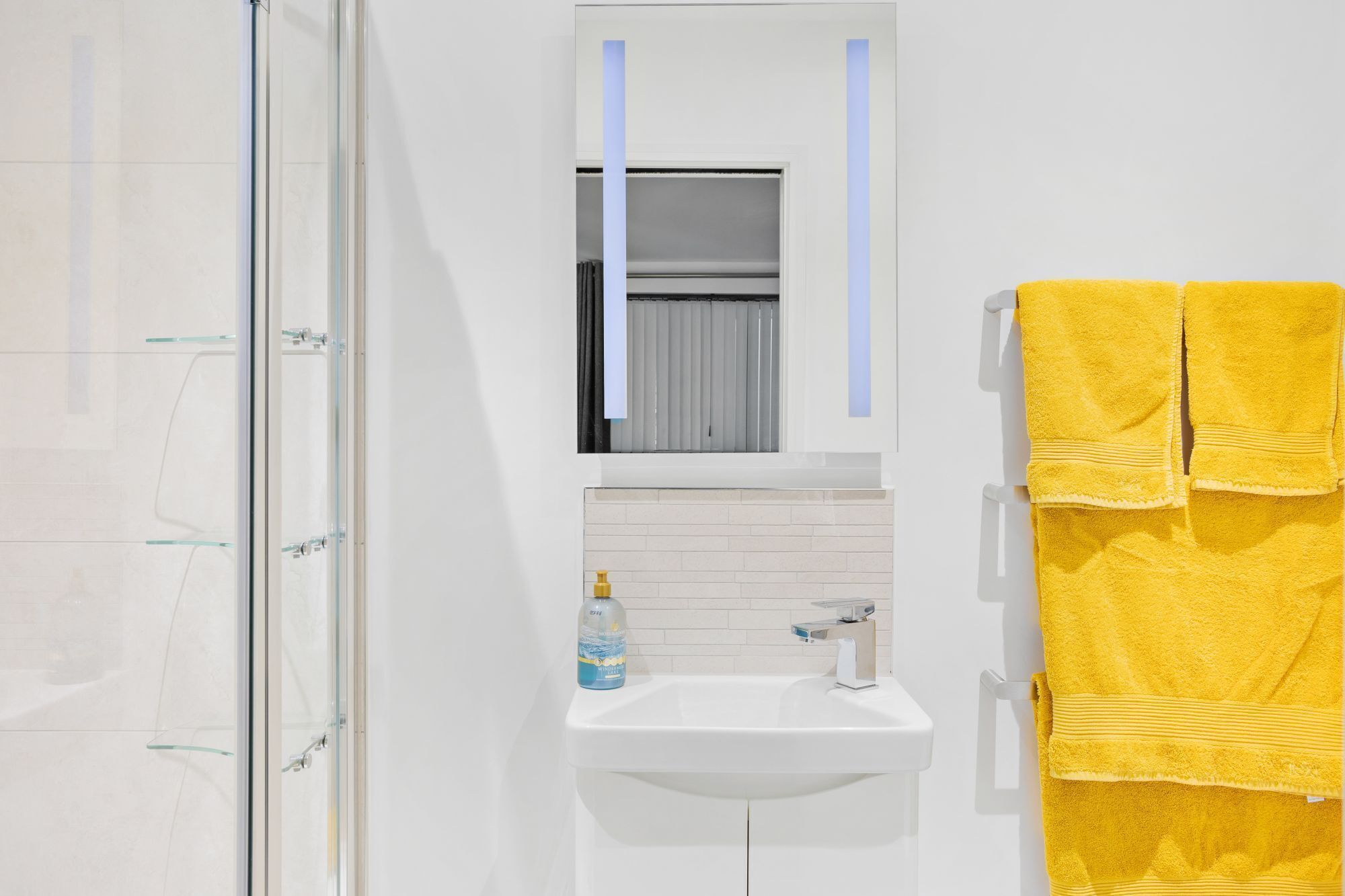 Ein Badezimmer mit Duschkabine aus Glas, einem weißen Waschbecken, einem Spiegel und einem gelben Handtuch.