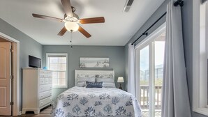Een slaapkamer met een bed, een plafondventilator, een dressoir, een raam en uitzicht op de omgeving.
