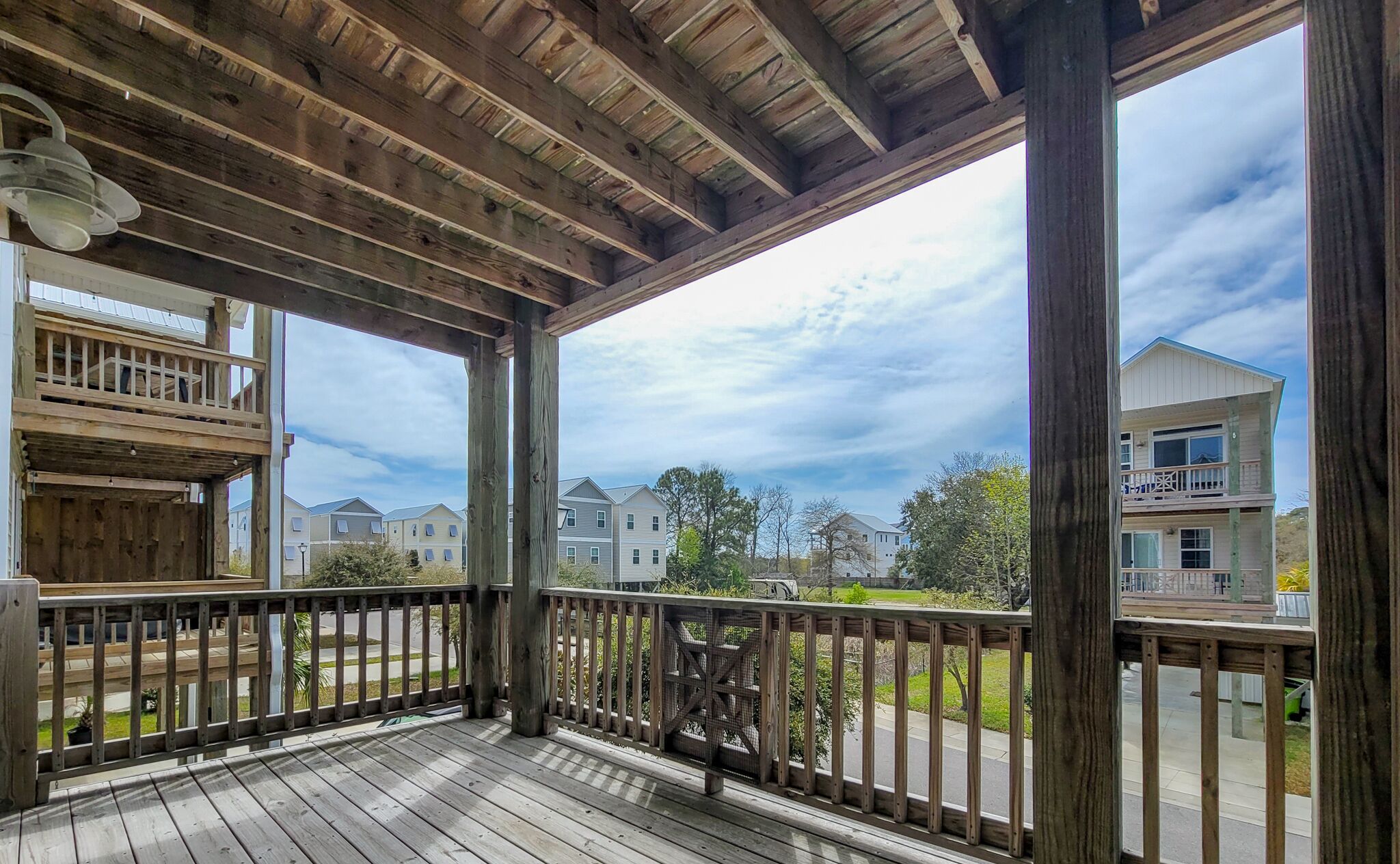 A wooden deck with a railing, overlooking a residential area with houses and a clear sky.