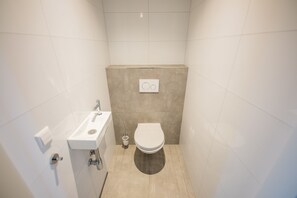Modern bathroom with a white toilet, sink, and chrome faucet, set against a clean, tiled backdrop.