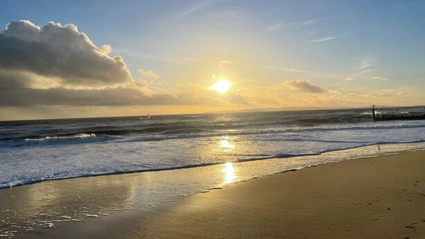 Uma praia com ondas, céu claro e um pôr do sol.