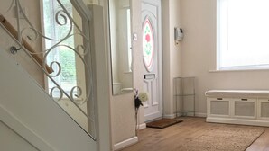 Um corredor com piso de madeira, uma porta branca com espelho decorativo e uma janela grande com persianas.
