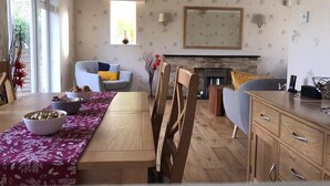 Uma sala de estar moderna com lareira, um espaço de jantar com mesa e cadeiras de madeira, e uma cozinha com armários de madeira.