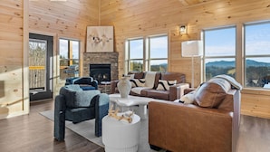 A spacious living room with a fireplace, large windows, and a view of the outdoors. - VIEWS FROM THE MOUNTAIN TOP is Ready for Company (SEVIERVILLE)