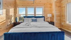 A wooden cabin bedroom with a large bed, two bedside tables, and a window with a view. - VIEWS FROM THE MOUNTAIN TOP is Ready for Company (SEVIERVILLE)