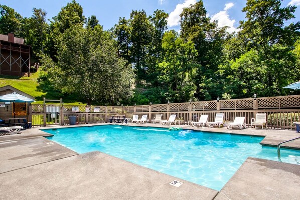 A swimming pool with lounge chairs and a wooden fence, surrounded by trees.