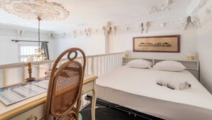 Una habitación de hotel con cama, escritorio, silla, candelabro y un cuadro en la pared.