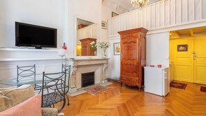 Una sala de estar con chimenea, televisor, mesa de comedor con sillas y una zona de cocina con puerta amarilla.