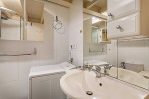 Ένα σύγχρονο μπάνιο με λευκό νιπτήρα, καθρέφτη και ένα διαχωριστικό από γυαλί για το ντους.