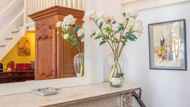 Una consola de mármol con un florero de flores blancas y una naturaleza muerta enmarcada.