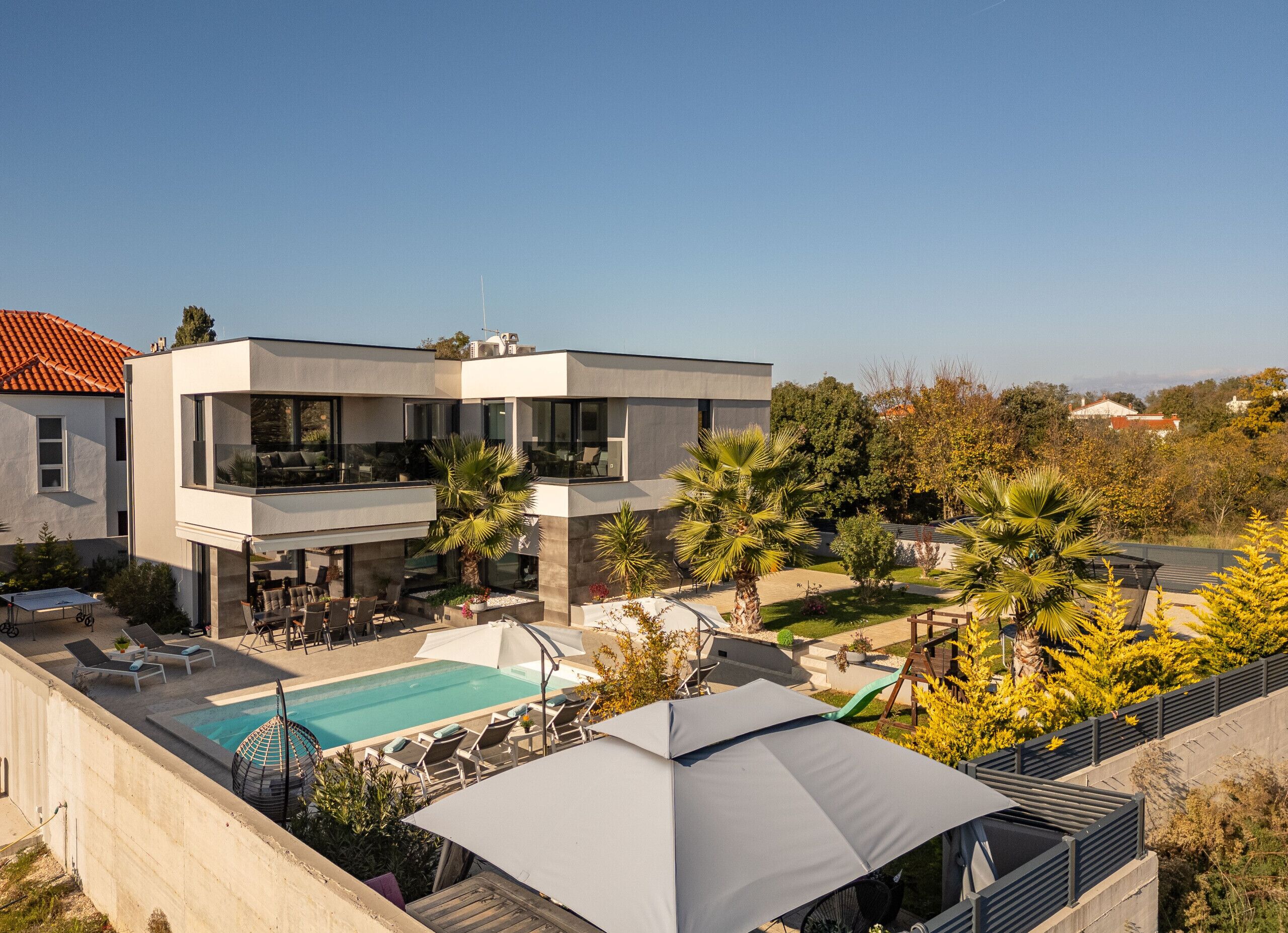 A modern two-story building with a rooftop pool, outdoor seating, and a large umbrella.