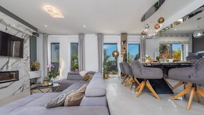 Un salon moderne doté d’un grand canapé d’angle, d’un coin repas avec une table et des chaises en bois, et d’un téléviseur à écran plat fixé à un mur en marbre.