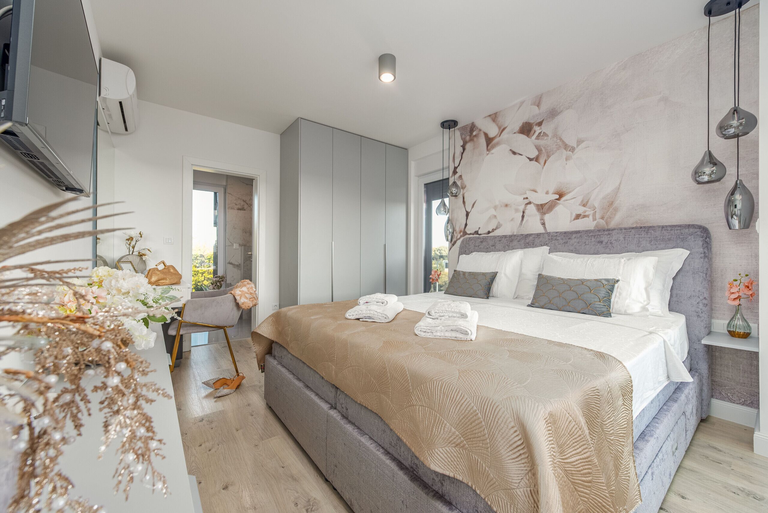 A modern bedroom with a large bed, a wardrobe, and a vanity with a mirror.