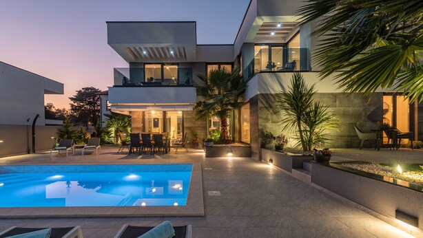 Une maison moderne à deux étages, dotée d’une piscine, d’un espace extérieur aménagé et d’un patio bien éclairé.